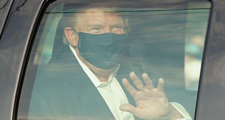 Donald Trump syns genom en bilruta. Han har mask för näsa och mun och vinkar.