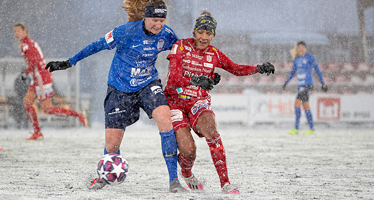 En match i fotboll. Två spelare kämpar om bollen. Det faller snö. Och det är snö på planen.