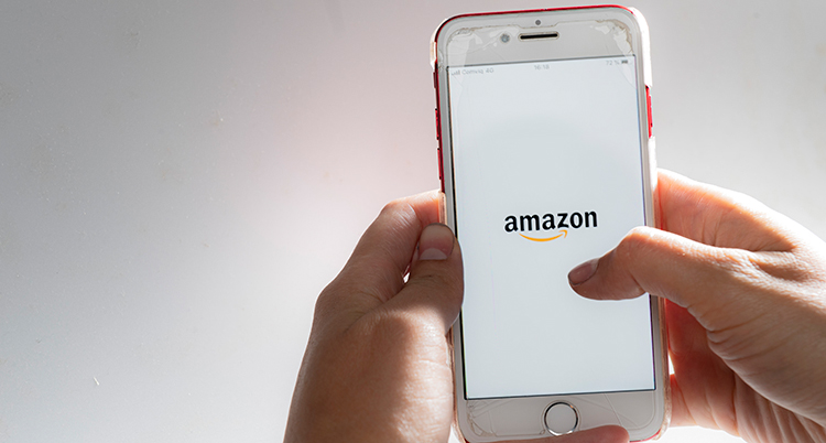 Händer som håller i en mobil som visar företaget Amazons namn