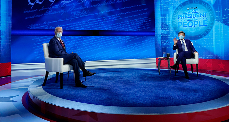 Bilden visar en stor tv-studio. Joe Biden sitter på en stol till vänster. En journalist sitter i en stol flera meter ifrån honom. Joe Biden har munskydd på sig.