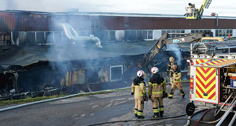 Tre brandmän står utanför stationen. Massor av rök syns runt den huset som är svart av sot.