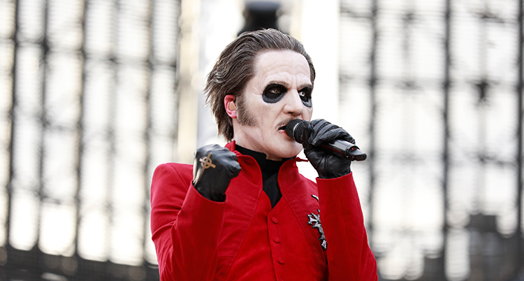 En man med vitsminkat ansikte och en röd jacka håller i en mikrofon. Hans högra näve är knuten och har en handske.