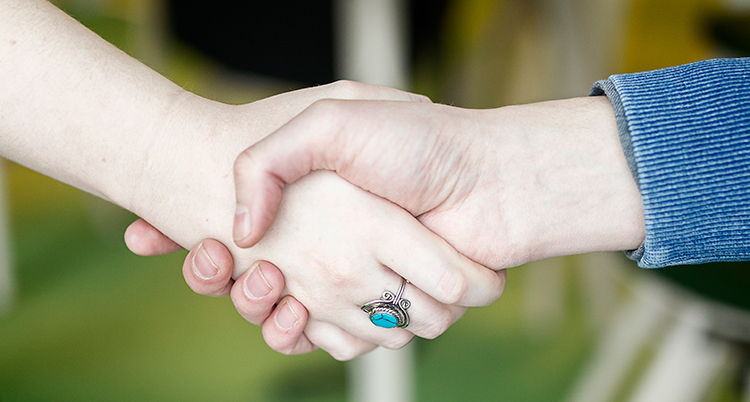 Ett handslag mellan en kvinna med en ring på fingret och en man med en blå jacka