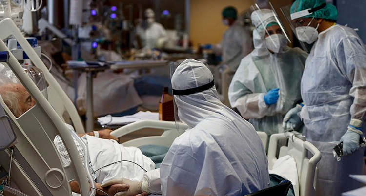 sjukvårdspersonal i visir står runt en säng på ett sjukhus