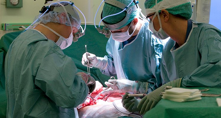 Tre läkare står runt ett operatonsbord och opererar.