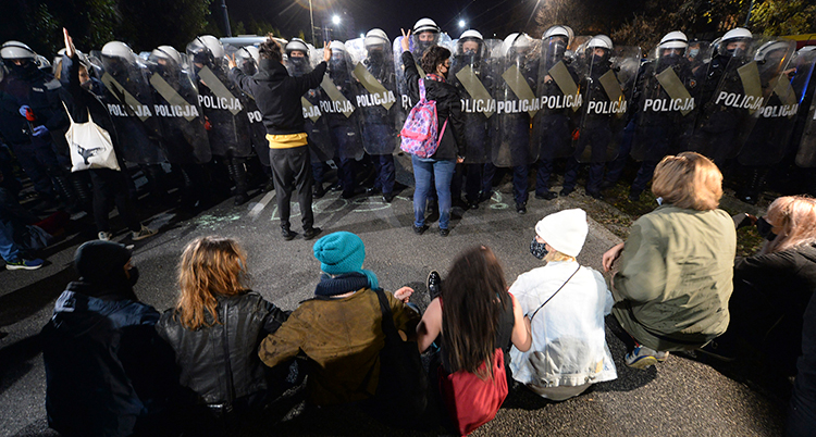 Kvinnor sitter på marken för att protestera. Mitt emot står kravalklädda poliser på rad.