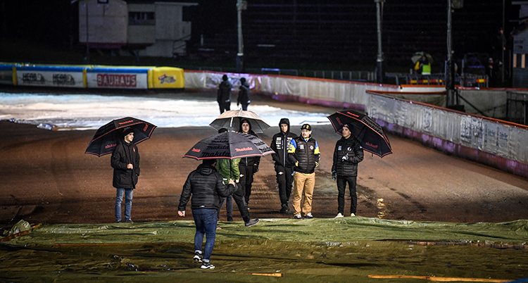 Människor står med paraplyer på en speedwaybana.