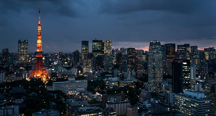 En vy över Tokyo på natten. Skyskrapor och ett vackert byggnadstorn syns. Det lyser i fönstren.