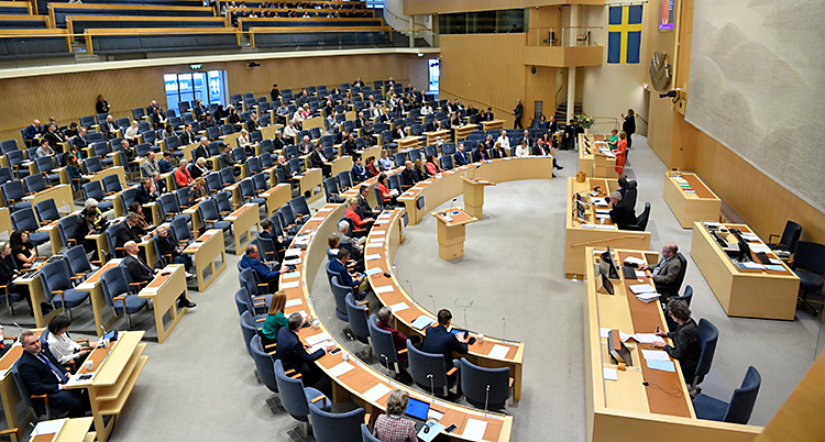 Stolar i riksdagen står i halvmåneformade rader mot ett podium.