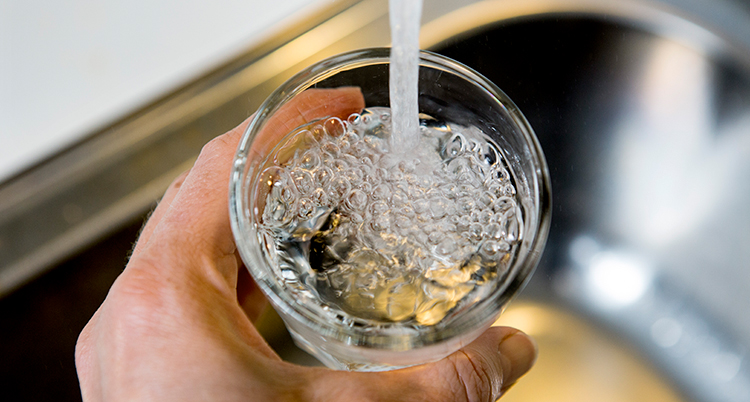 En hand håller i ett glas som fylls på med vatten från en kran.