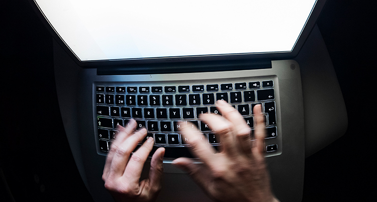 Ett par händer skriver på ett tangentbord. Datorns skärm syns också