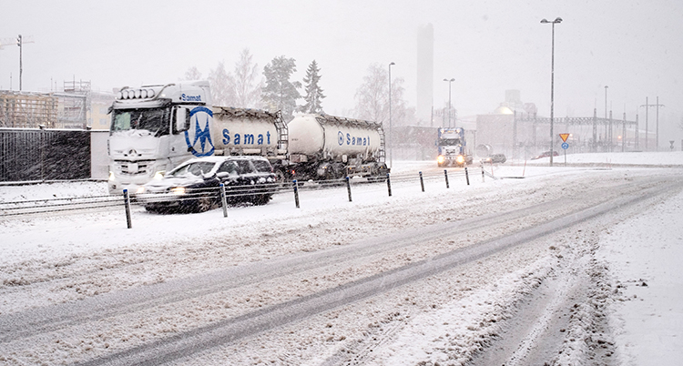Bilar och en stor lastbil åker på en väg med massor av snö.