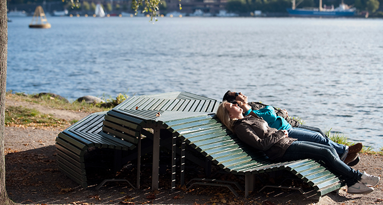 Två personer ligger på en bänk utomhus och solar.