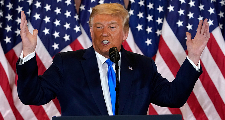 Trump ser allvarlig ut och håller ut armarna. Bakom honom är en amerikansk flagga.
