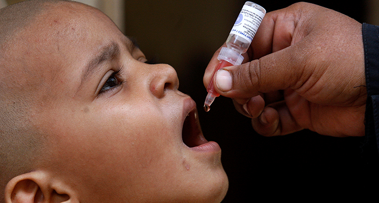 Ett barn gapar och över munnen håller en vuxen hand en vaccinationsspruta