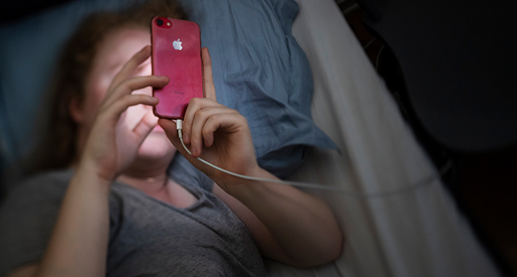En kvinna ligger i sängen och tittar i mobilen.