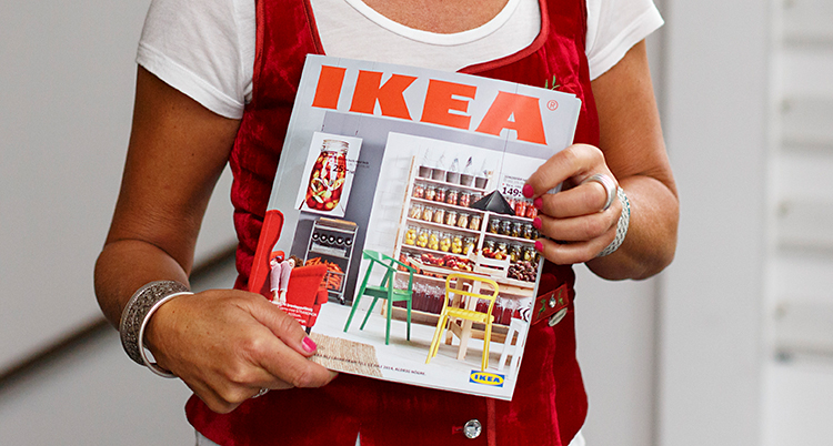 En kvinna står och håller i en katalog. Det står Ikea på katalogen med röda bokstäver.