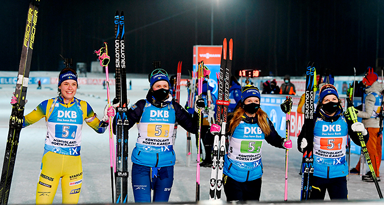 Fyra kvinnor står bredvid varandra. De håller i sina skidor. De är glada. De har vunnit.