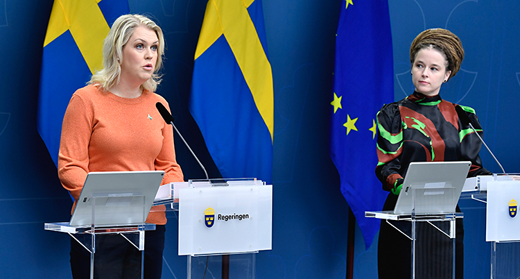 Hallengren pratar i en mikrofon. Balkom henne är en svensk flagga.