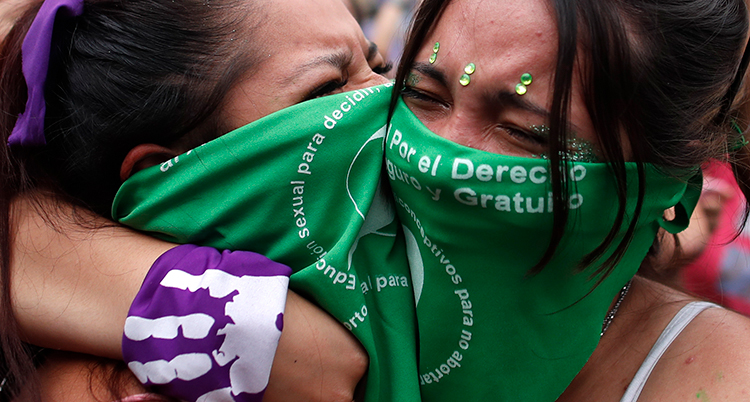 Två kvinnor med gröna sjalar för munnen kramar om varandra