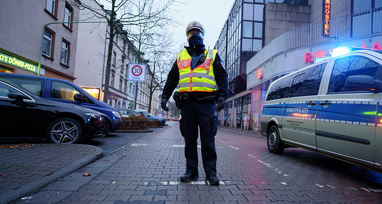 En polis i gul varselväst står mitt i gatan, en polisbil passerar till höger