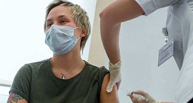 En kvinna med munskydd får en spruta i armen.