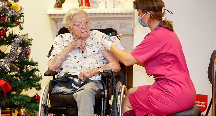 En sjuksköterska i rosa kläder ger en spruta till en kvinna som sitter i rullstol