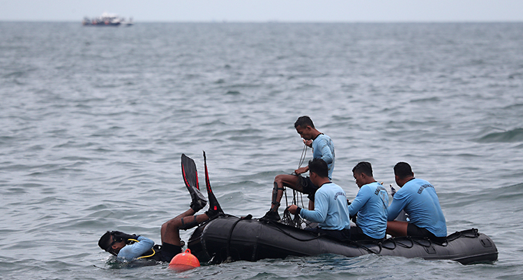 Bilden är tagen i havet utanför landet Indonesien. Några män sitter i en liten båt. En av män är på väg att dyka ner i havet.