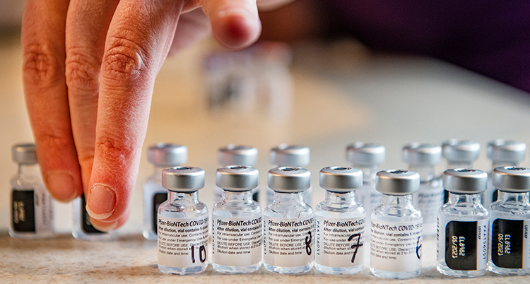 En hand över flera små flaskor med vaccin.