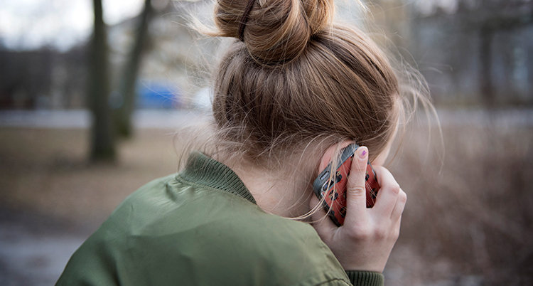 Ett barn håller i en telefon mot örat. Hon sitter utomhus.