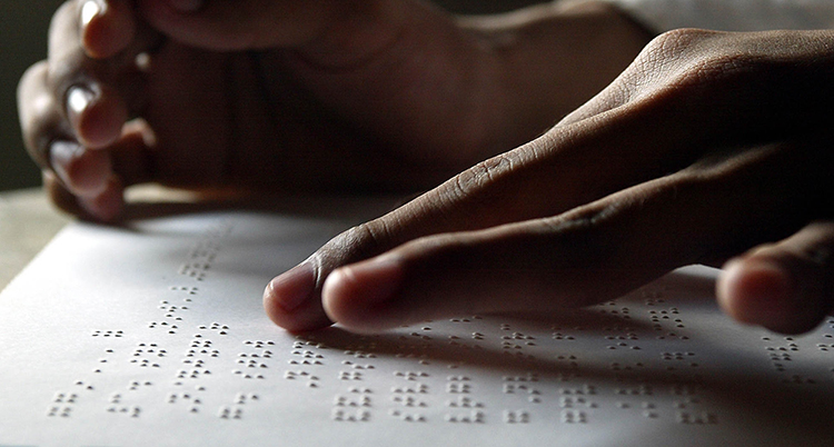 Fingertoppar läser av en text i punktskrift i form av upphöjda punkter på ett vitt papper