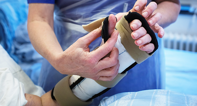 En skötare håller i en hand i stödskena och bandage.
