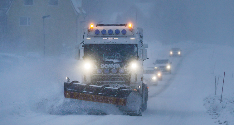 Det snöar mycket. Lastbilen kör på vägen.