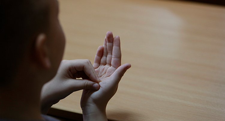 En pojke gör ett tecken i teckenspråk. Han sätter ihop alla fingrarna i sin vänstra hand. Och sedan trycker han dem mot handflatan i sin högra hand.