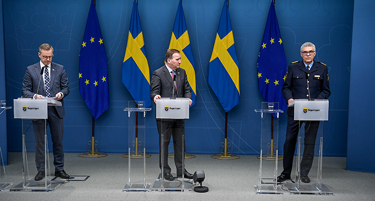 Tre män står och pratar i varsin mikrofon. I bakgrunden finns svenska flaggor.