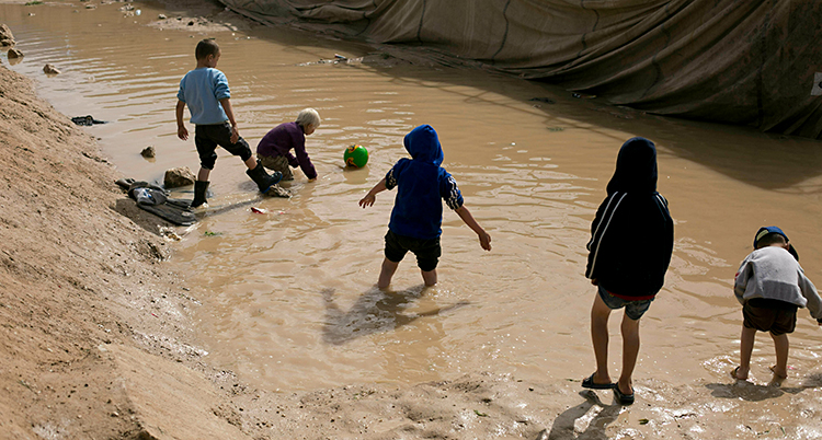 Fem barn leker i ett smutsigt vatten. De har en fotboll.