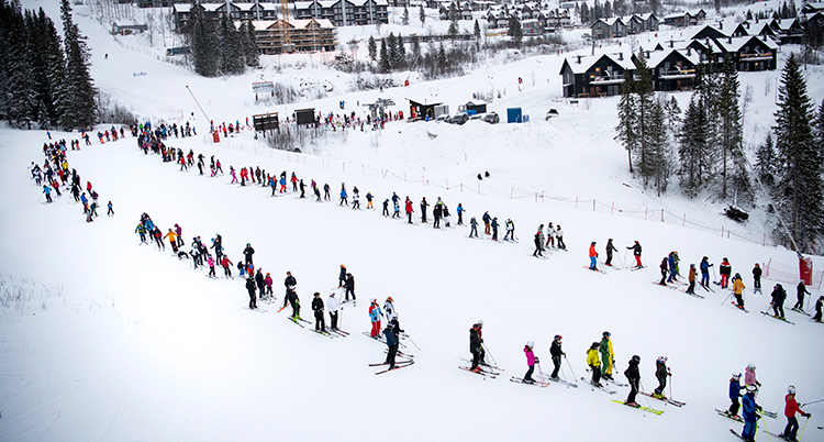 En flygbild. Flera hundra människor med skidor står i en lång kö. De har någon meters avstånd. I bakgrunden syns hus.