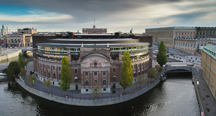 en bild ovanifrån på riksdagens byggnad. Omgiven av vatten och en vackert molnbeslöjad himmel.