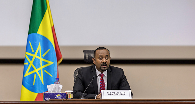Abay Ahmed sitter vid ett skrivbord. Han pratar i en mikrofon. Han har kostym och slips. I bakgrunden är Etiopiens flagga.
