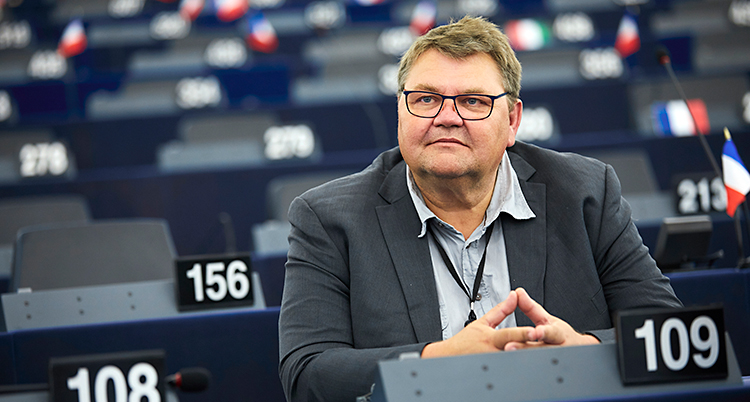 Peter Lundgren sitter i den stora salen i EUs riksdag. Han har kort hår och glasögon. Han har skjorta och kavaj.