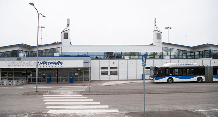 Ett vitt övergångsställ över gatan och på andra sidan syns entrén till flygplatsterminalen.