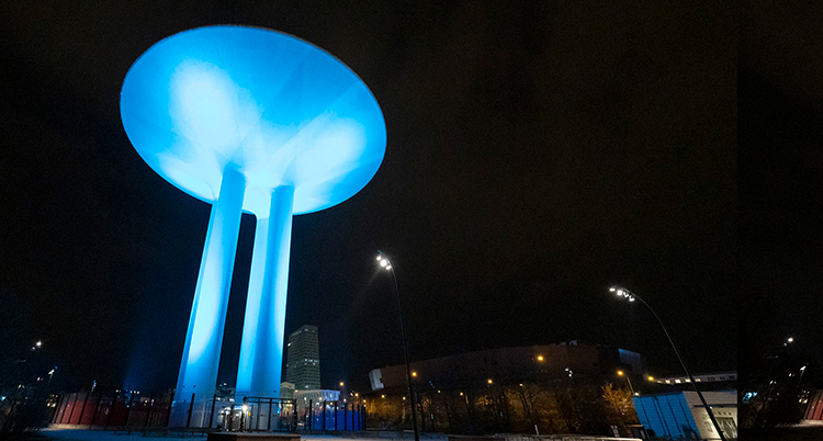 Ett vattentorn är upplyst i blått mot en svart stad.