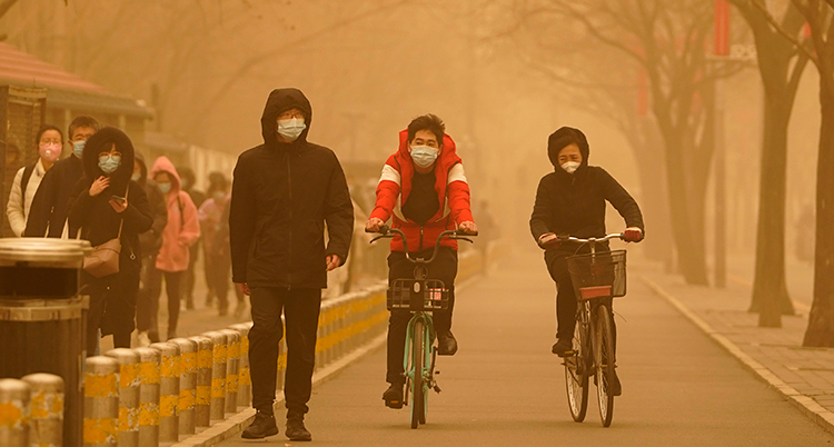 Luften är gul, människor går och cyklar på en gata och de har munskydd