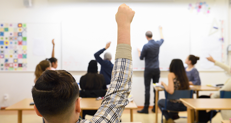 En elev räcker upp handen i ett klassrum.