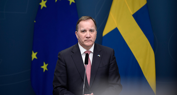 Han talar i en mikrofon. Bakgrunden är en EU-flagga och en svensk flagga.