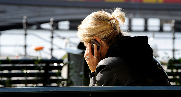 En kvinna sitter på en bänk och talar i telefonen. Hon syns bakifrån.