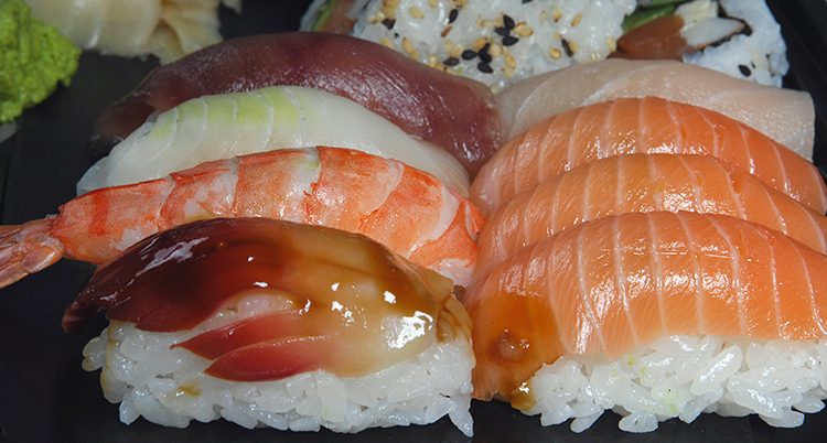 Flera bitar sushi ligger upplagda, de är gjorda av vitt ris med lax ovanpå.