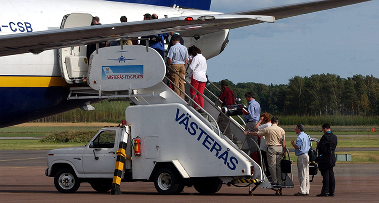 Människor går ombord på ett flygplan med hjälp av en trappa på flaket på en bil.