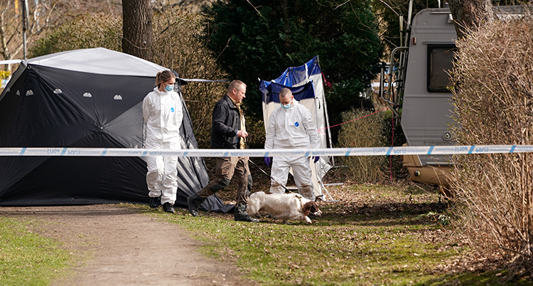 Poliser i vita overaller bakom en avspärrning utomhus.