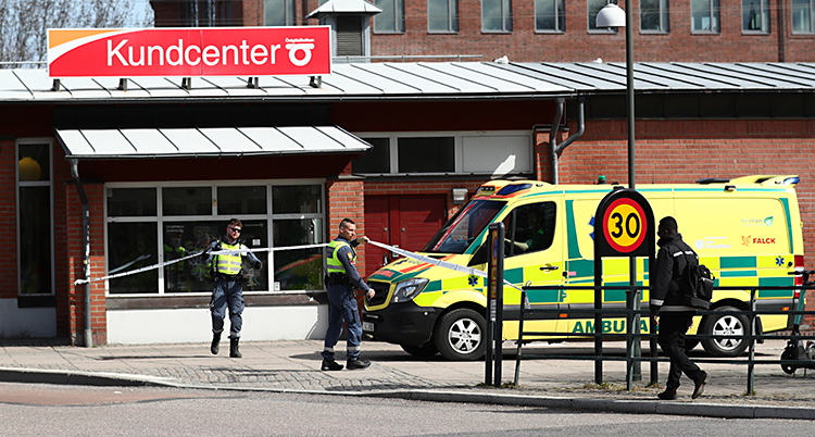 En bild som är tagen utomhus, i Linköping. Två poliser står vid ett avspärrningsband. En ambulans står bredvid. Bakom finns ett hus där det står Kundcenter på taket.